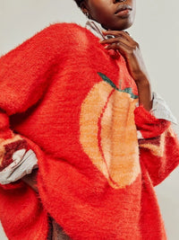 Person wearing a red sweater with a pumpkin design on a plain background