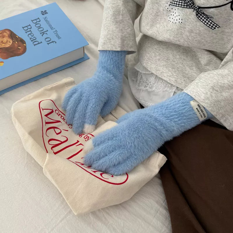 Person wearing blue fuzzy gloves holding a book on a surface with a bag and another book.