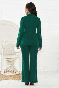Woman wearing a green suit standing in a minimalistic room with a white chair.
