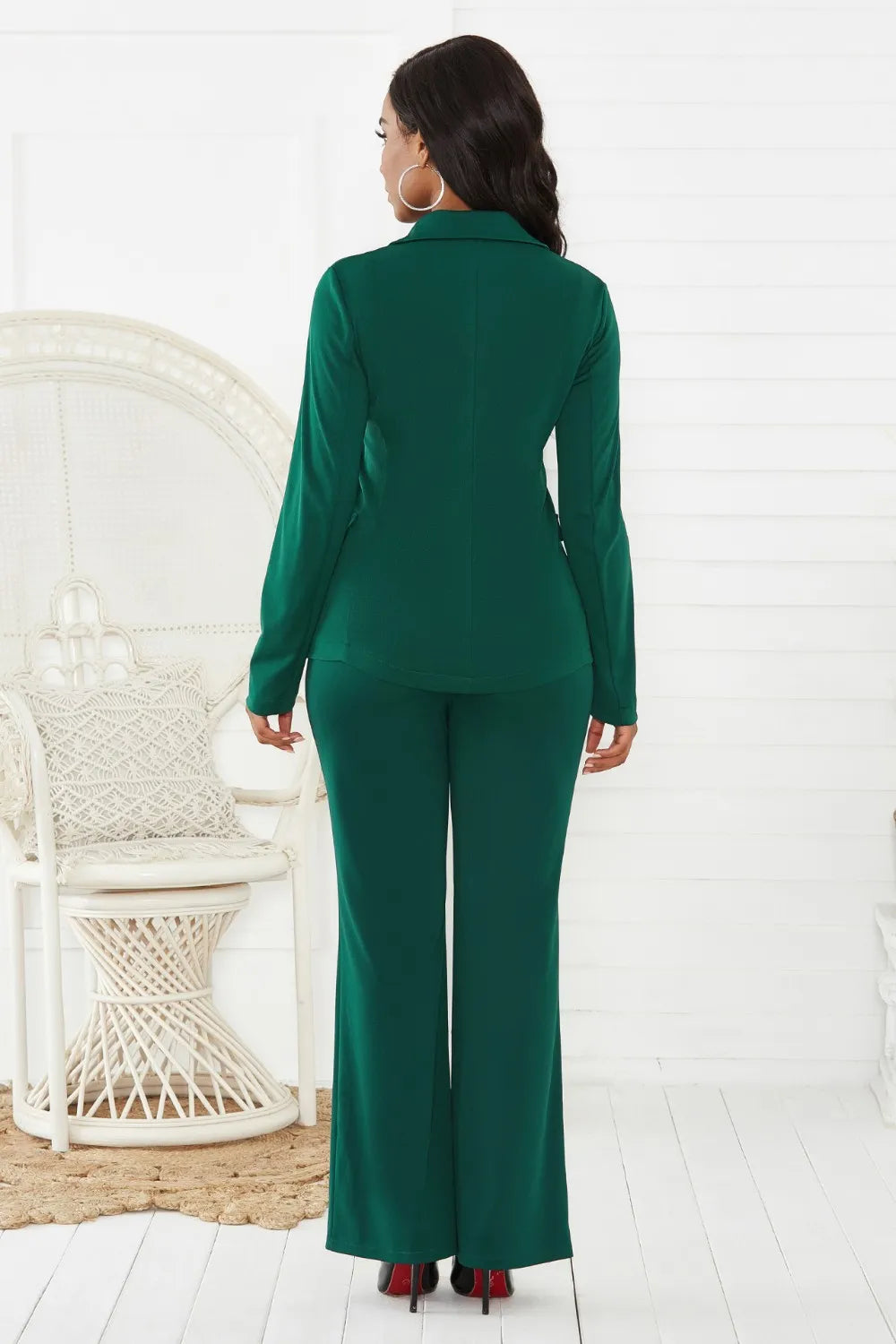 Woman wearing a green suit standing in a minimalistic room with a white chair.