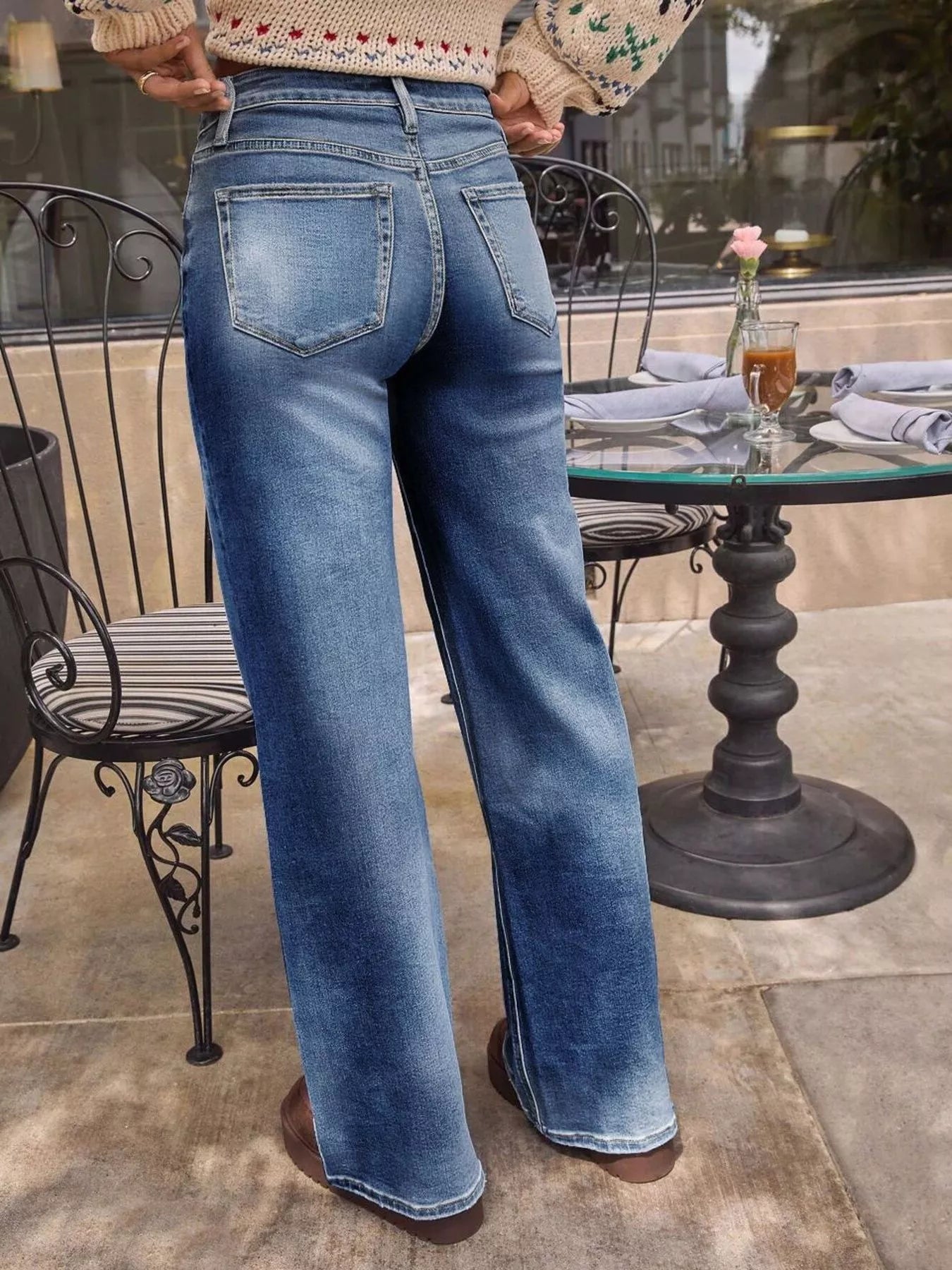 Person wearing blue jeans standing outdoors near a table with a glass top.