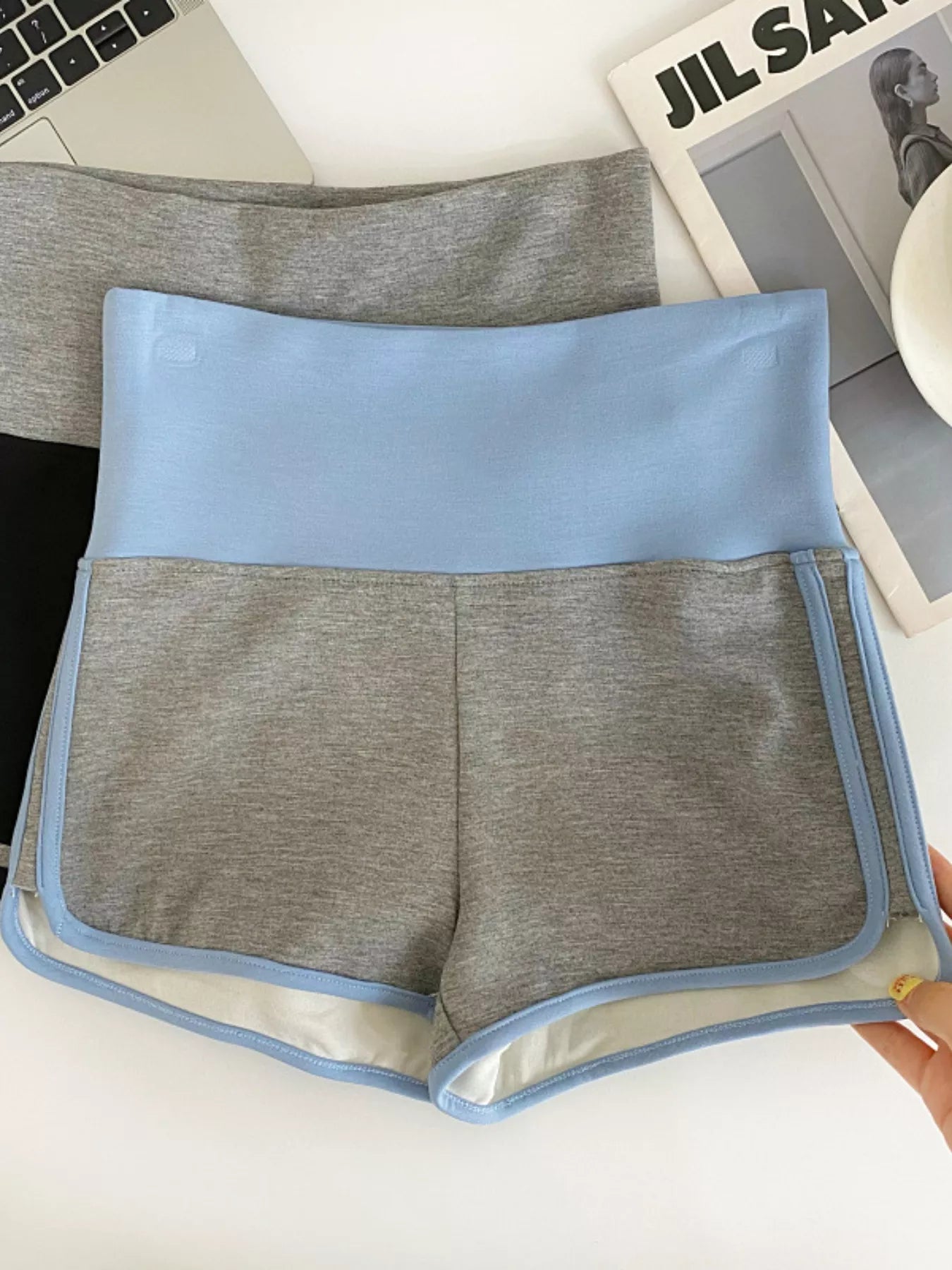 Gray shorts with blue trim held in front of a laptop and magazine.