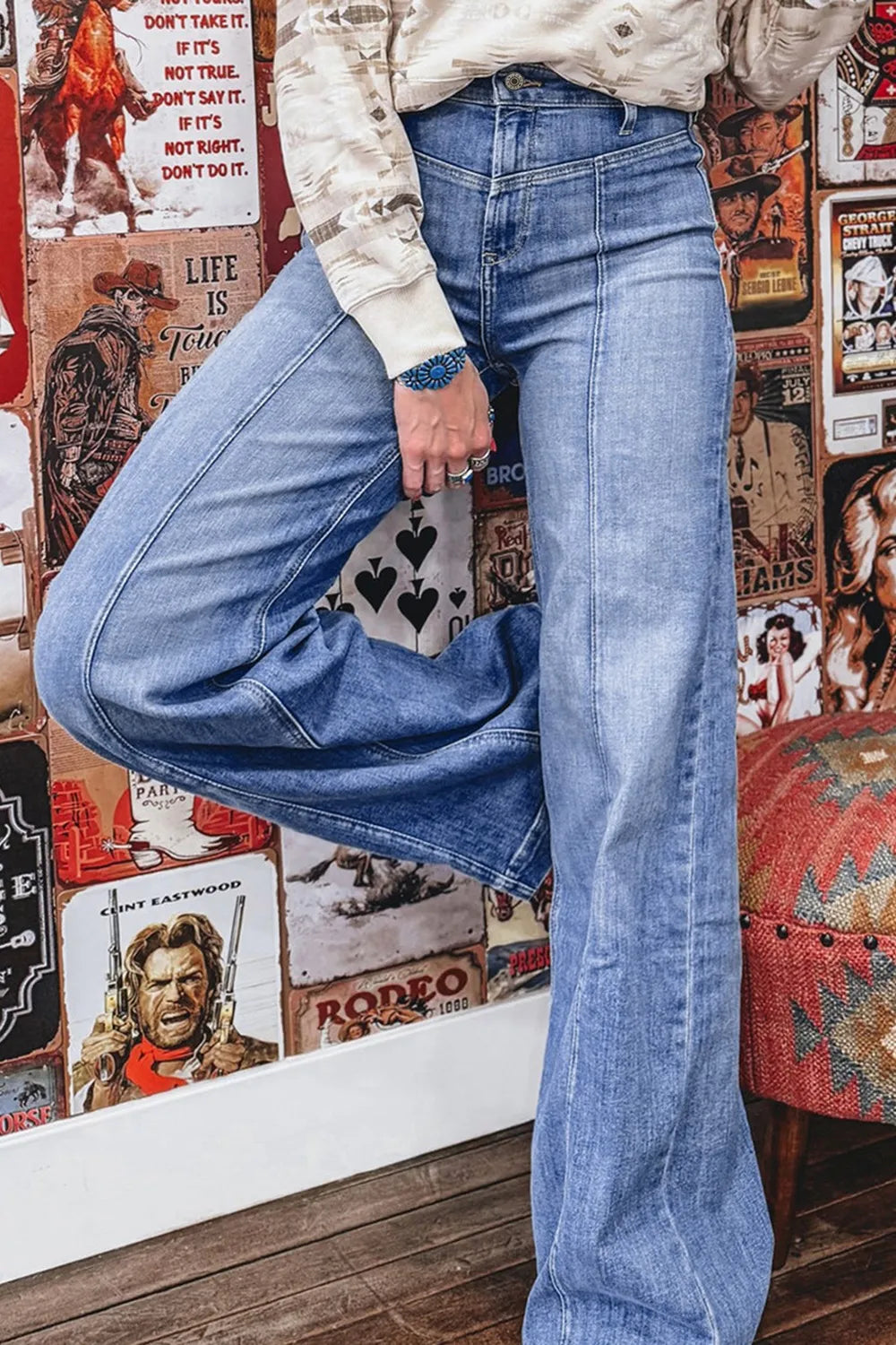 Person wearing blue jeans standing in front of a wall with vintage posters.