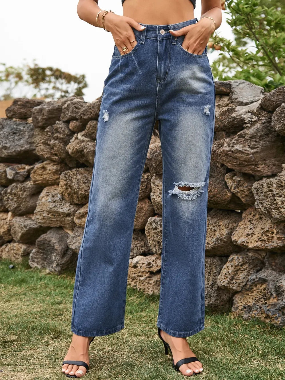 Person wearing blue jeans with a stone wall and grass background