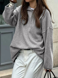 Person wearing a gray sweater and white pants walking outdoors.