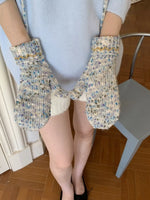 Person wearing colorful knitted mittens on a wooden floor.