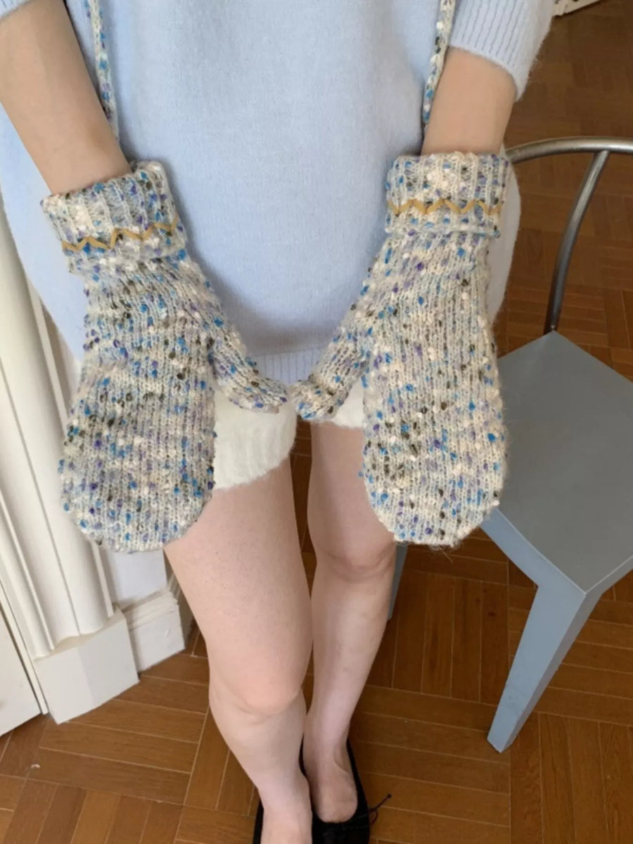Person wearing colorful knitted mittens on a wooden floor.