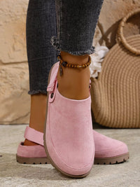 Pink suede clogs worn with jeans on a neutral background