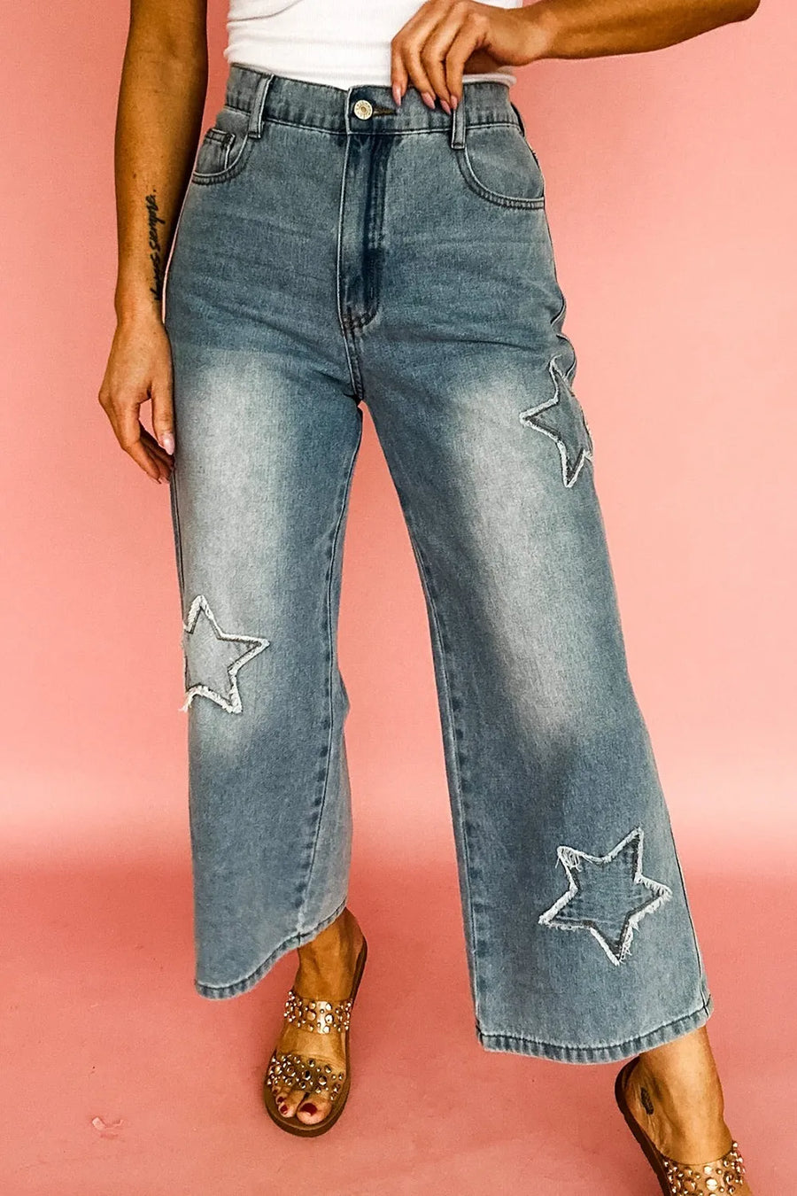 Person wearing blue jeans with star patches on a pink background
