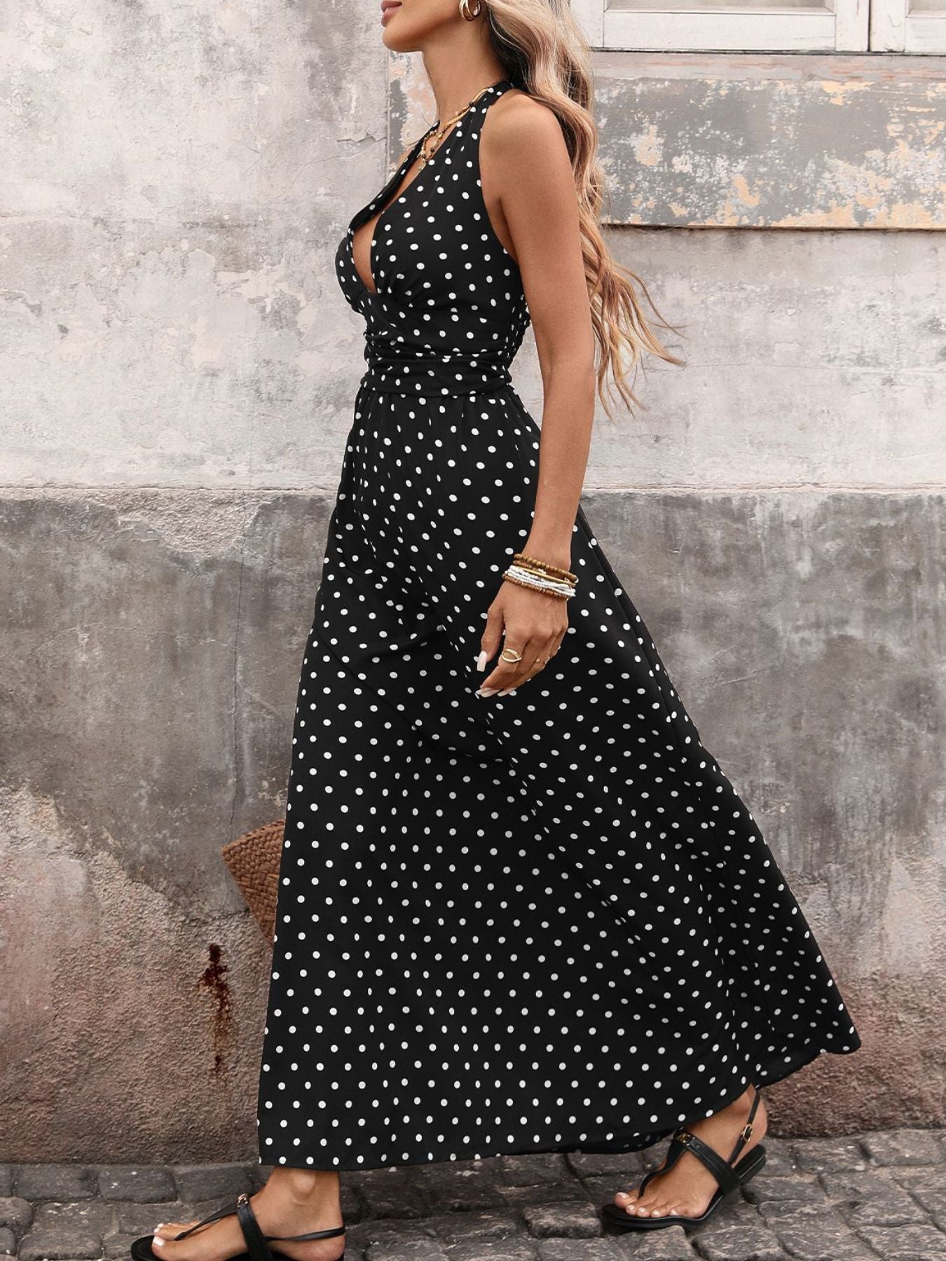 Woman wearing a black polka dot dress against a textured wall.
