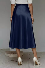 Person wearing a navy blue skirt and white shoes on a neutral background
