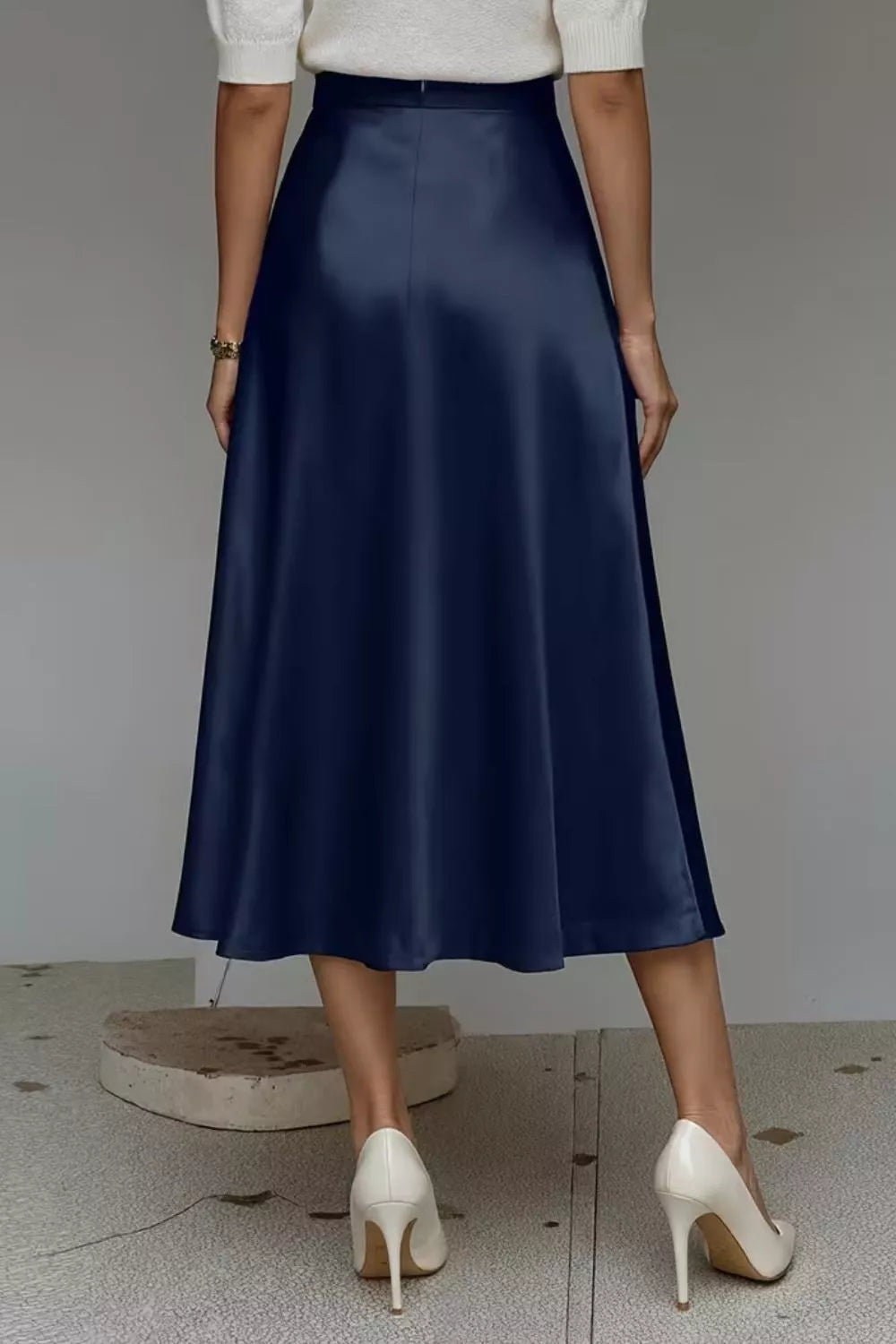 Person wearing a navy blue skirt and white shoes on a neutral background
