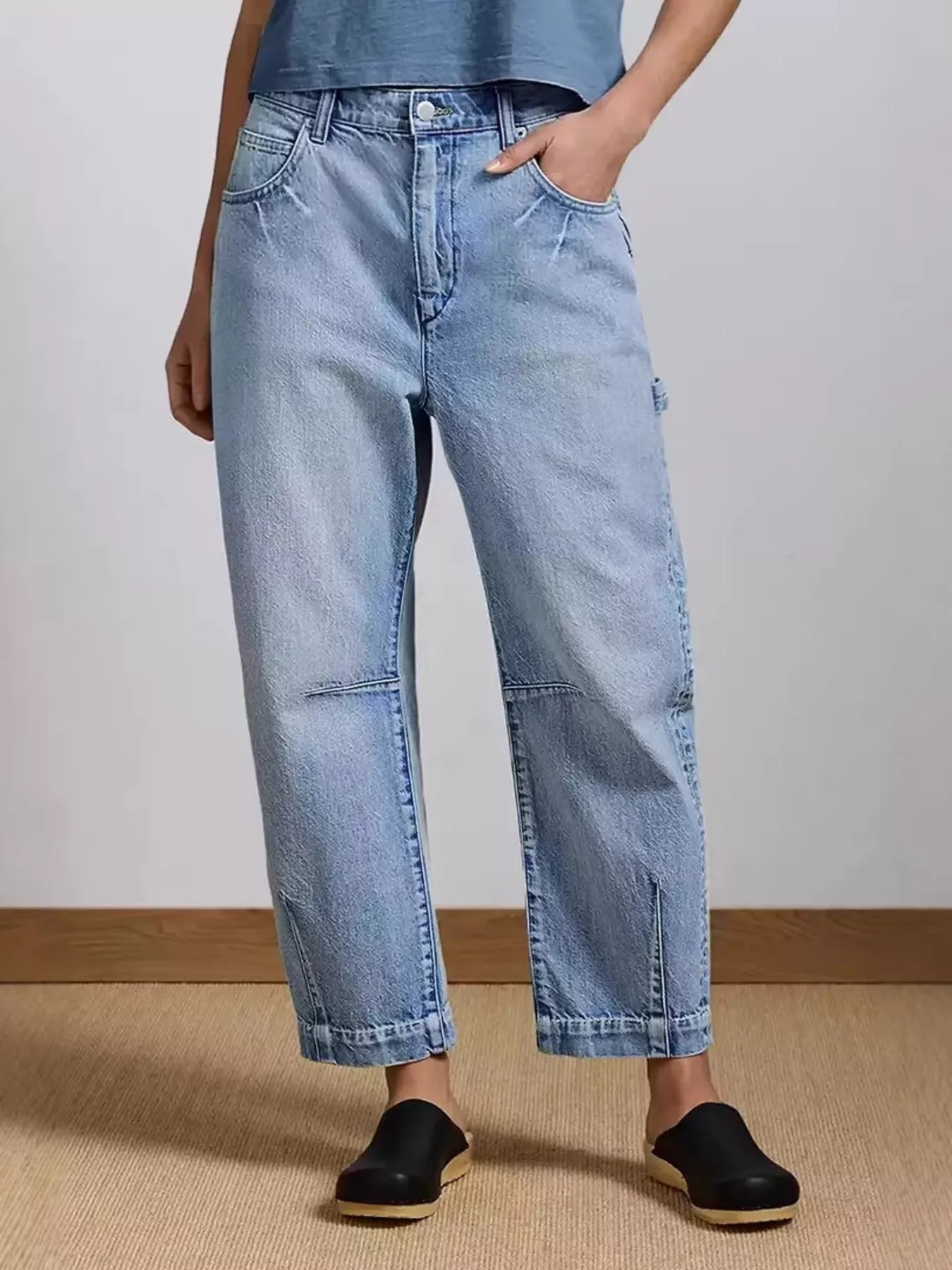 Person wearing light blue jeans and black shoes on a plain background