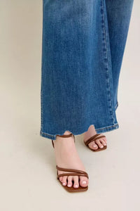Brown sandals worn with blue jeans on a neutral background