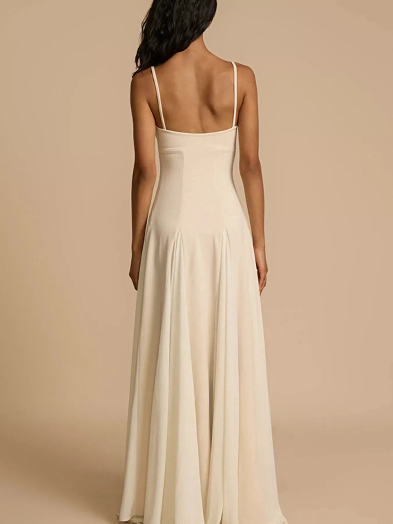 Woman wearing a long, light-colored dress with thin straps on a beige background