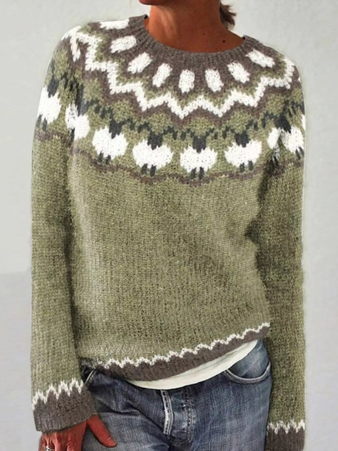 Person wearing a green knitted sweater with a white pattern on a plain background