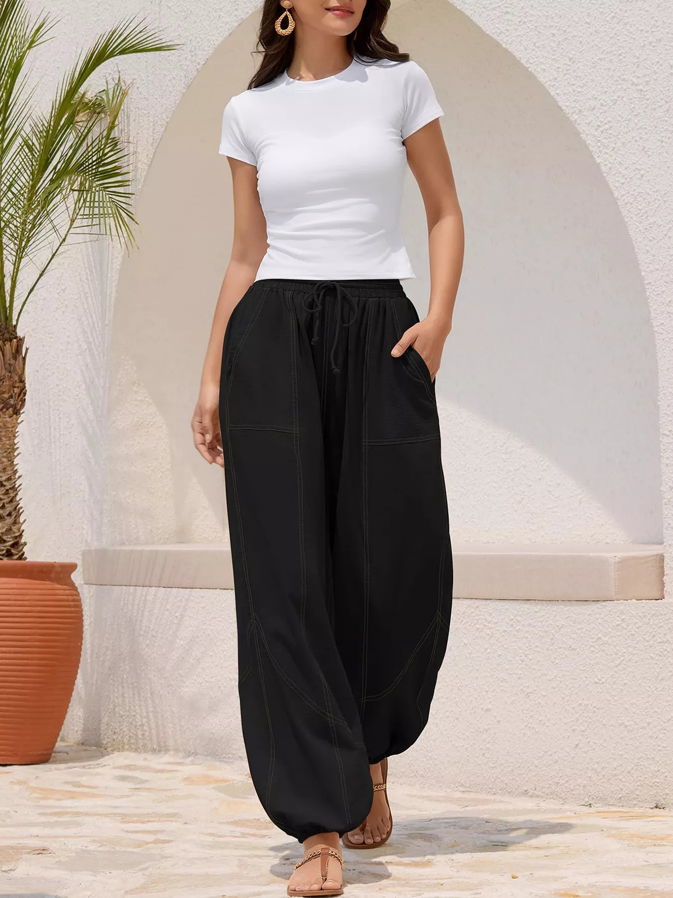 Woman wearing a white top and black wide-leg pants standing against a light-colored wall.