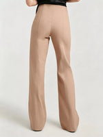 A person shown from the back wearing high-waisted, wide-leg trousers in a light tan or nude beige color, paired with a black top, against a plain light gray studio background.