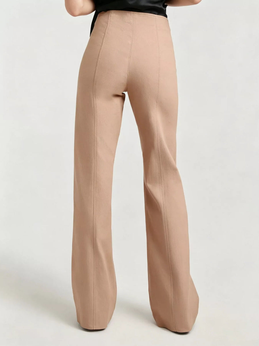 A person shown from the back wearing high-waisted, wide-leg trousers in a light tan or nude beige color, paired with a black top, against a plain light gray studio background.