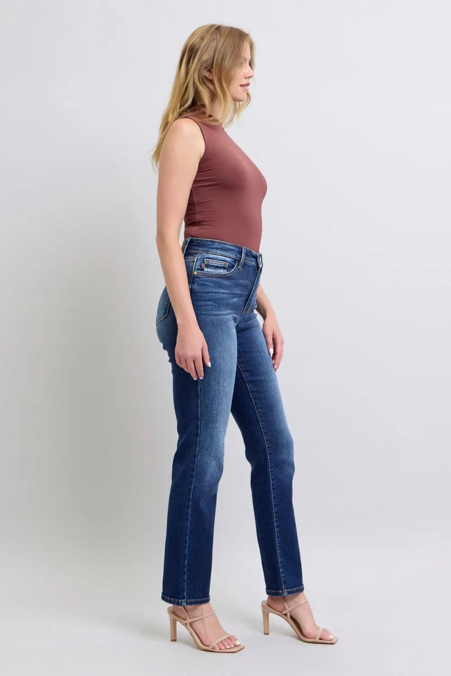 Woman wearing blue jeans and a brown top on a white background