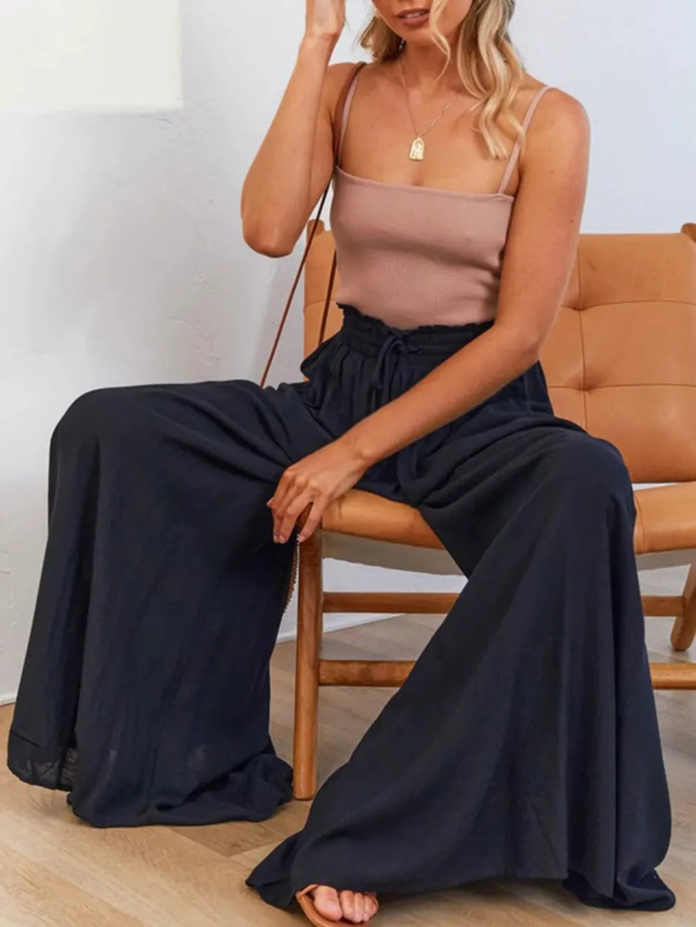 Woman sitting on a chair wearing a beige top and black wide-leg pants.