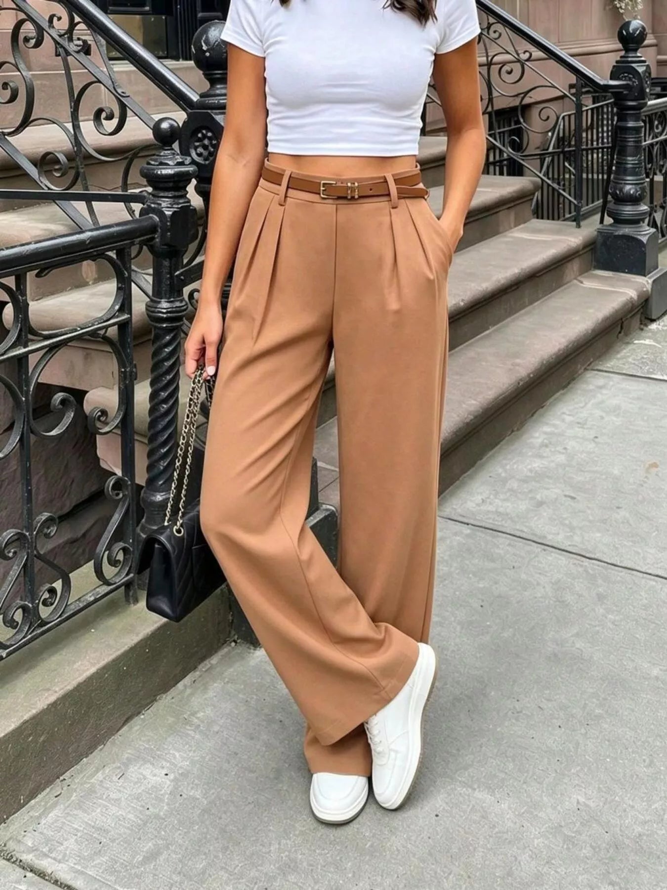 Person wearing a white top and tan wide-leg pants standing on a city street.