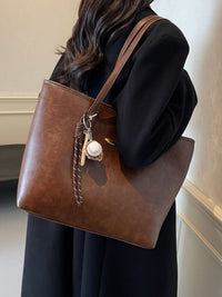 Brown leather tote bag with keychain held by a person wearing a black coat.