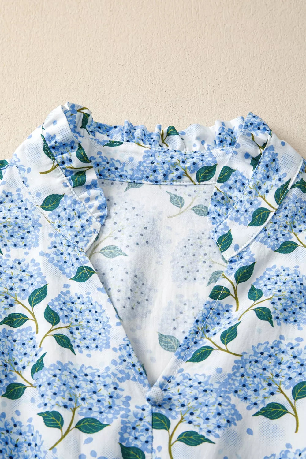 Close-up of a floral patterned fabric with blue flowers and green leaves on a beige background