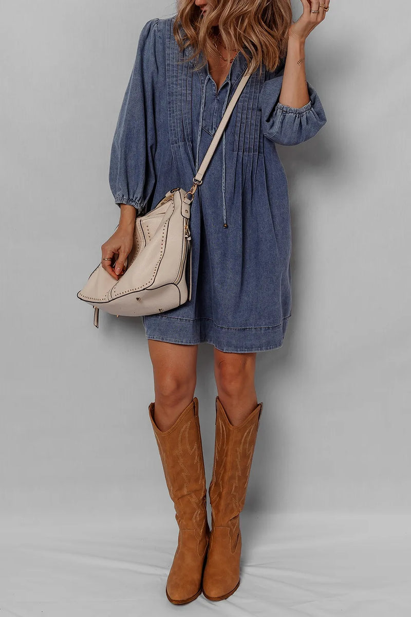 Person wearing a blue dress and brown knee-high boots with a beige handbag on a gray background