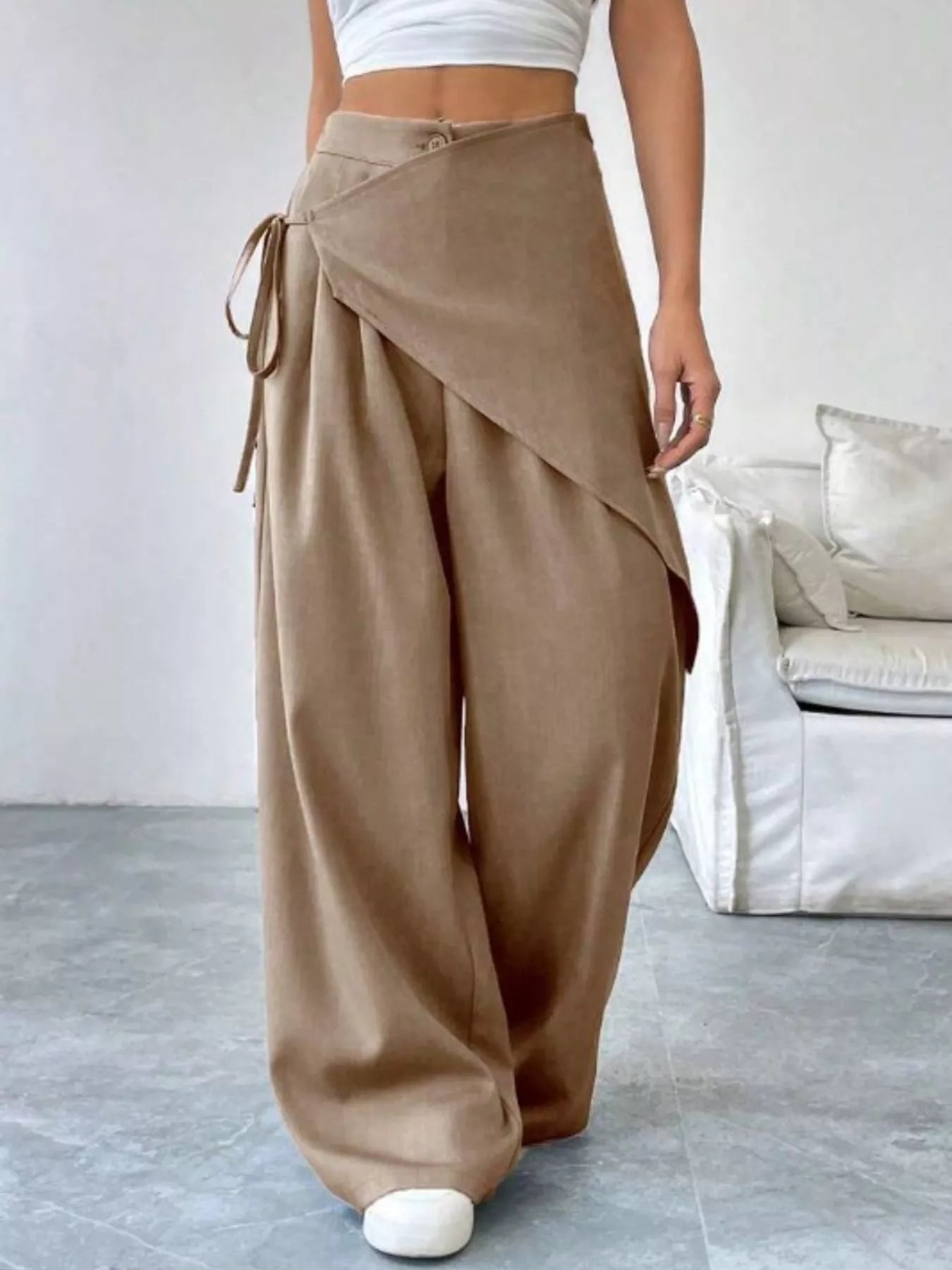 Person wearing brown wide-leg pants with a white top in a minimalistic room.