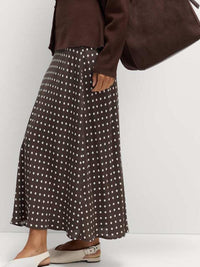 Person wearing a brown polka dot skirt with a plain background