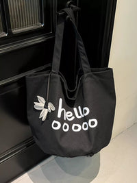 Black tote bag with 'hello ooooo' text and flower design hanging on a black door.