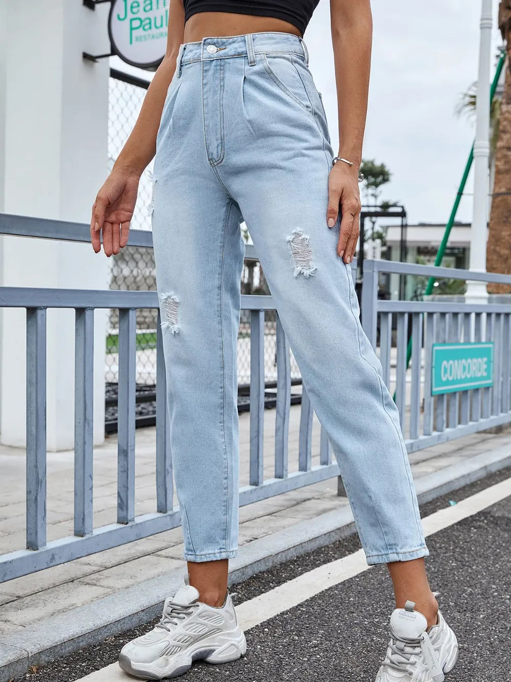 Person wearing light blue jeans with a slight crop, standing on a street.