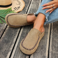 Beige loafers worn by a person on a wooden floor with a hat and plant in the background.