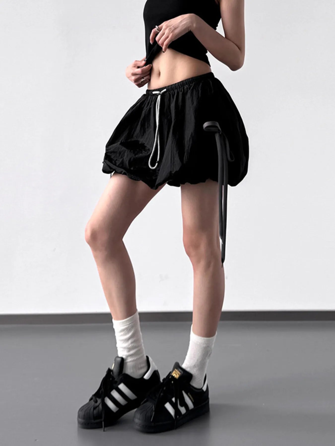 Person wearing black athletic shorts and Adidas shoes on a plain background