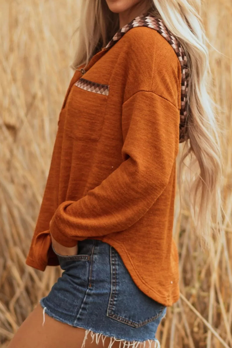 Person wearing an orange long-sleeve shirt and denim shorts standing in a field of tall grass.