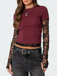 Person wearing a burgundy top with lace sleeves and black jeans on a white background