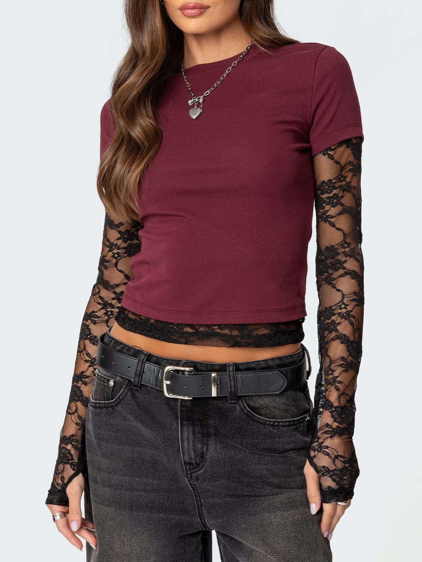 Person wearing a burgundy top with lace sleeves and black jeans on a white background