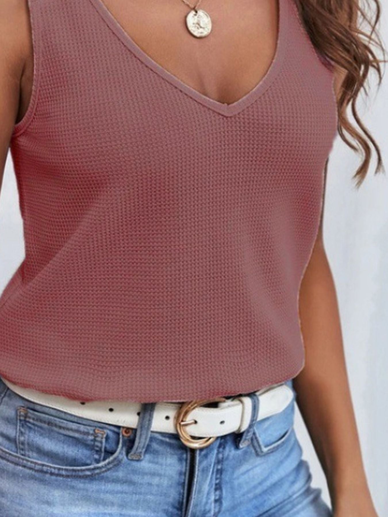 Person wearing a maroon tank top and blue jeans with a white background