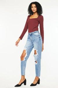 Woman wearing a burgundy long-sleeve top and light blue ripped jeans on a white background
