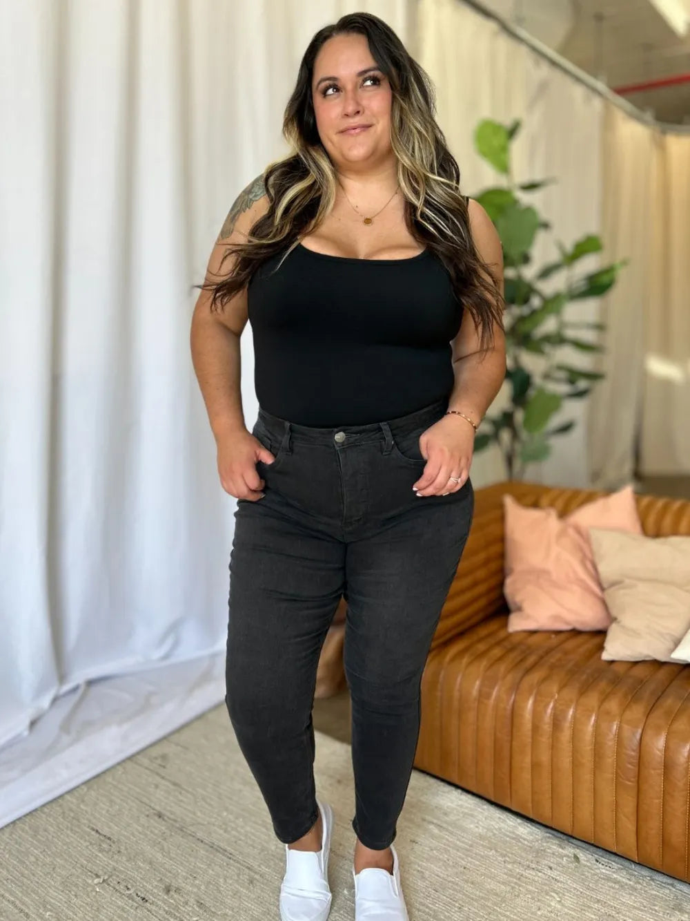 Woman wearing a black top and dark jeans standing in a living room.