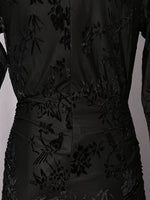 Close-up of a black long-sleeve dress with tonal floral and bird embroidery, showing the back waist and center seam.