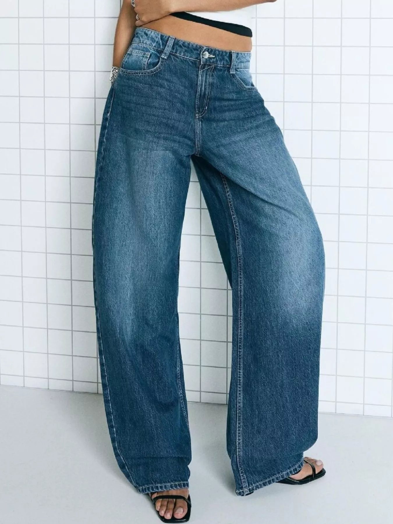 Person wearing wide-leg jeans against a white tiled wall.
