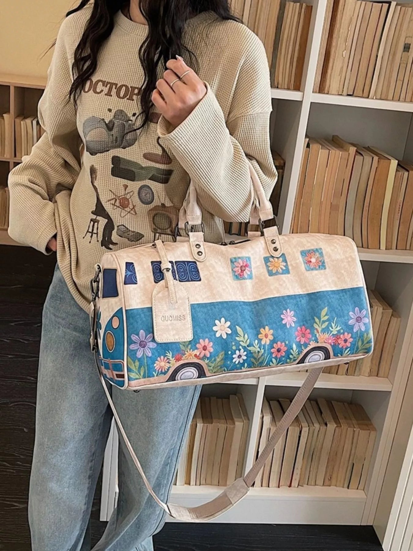 Person holding a floral and camper van-patterned bag in a room with bookshelves.