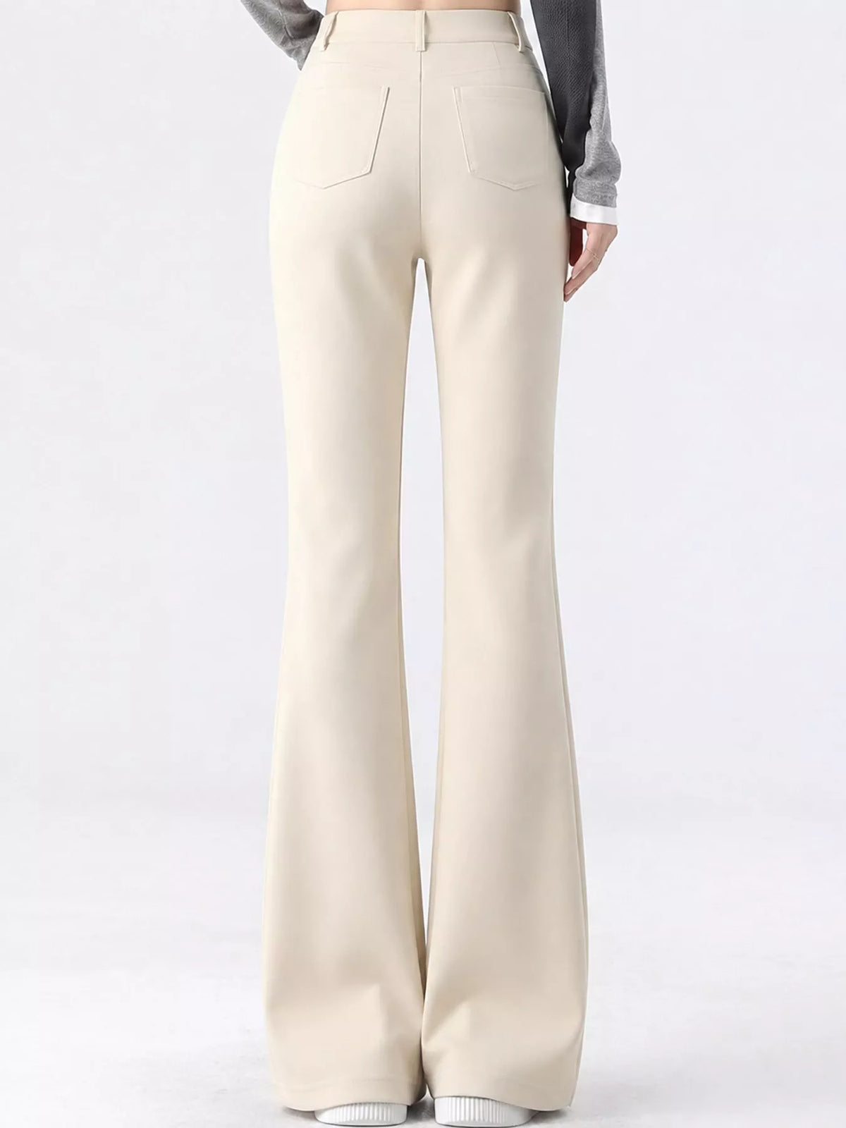 A person shown from the back wearing high-waisted, wide-leg cream pants with a gray long-sleeve top, set against a plain light gray studio background.