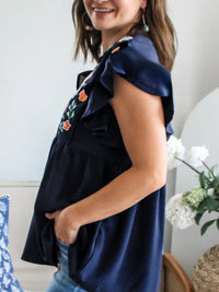 Woman wearing a navy blue top with floral embroidery in a casual setting.