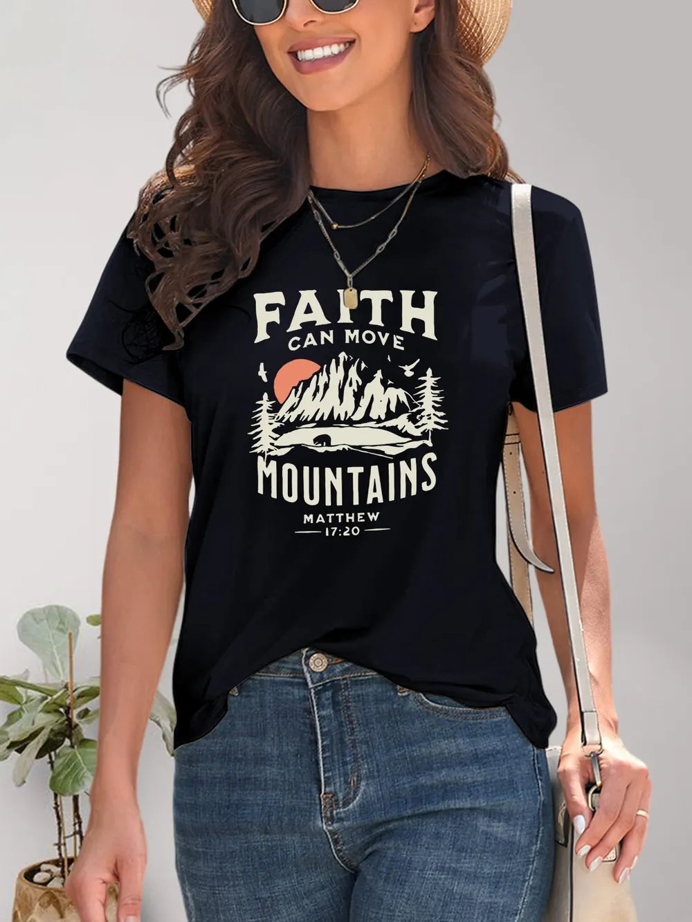 Woman wearing a black t-shirt with 'Faith Can Move Mountains' graphic and text.