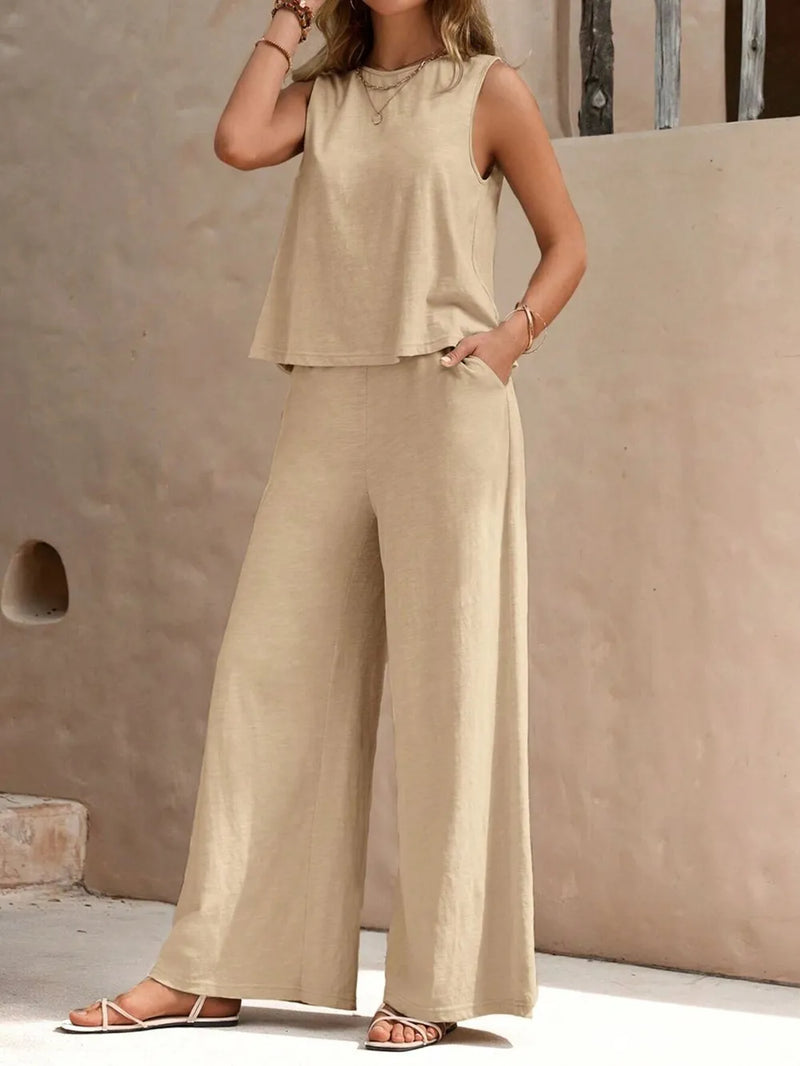 Woman wearing a beige sleeveless top and wide-leg pants against a neutral wall.