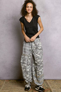 Person wearing a black top and patterned gray pants against a plain background