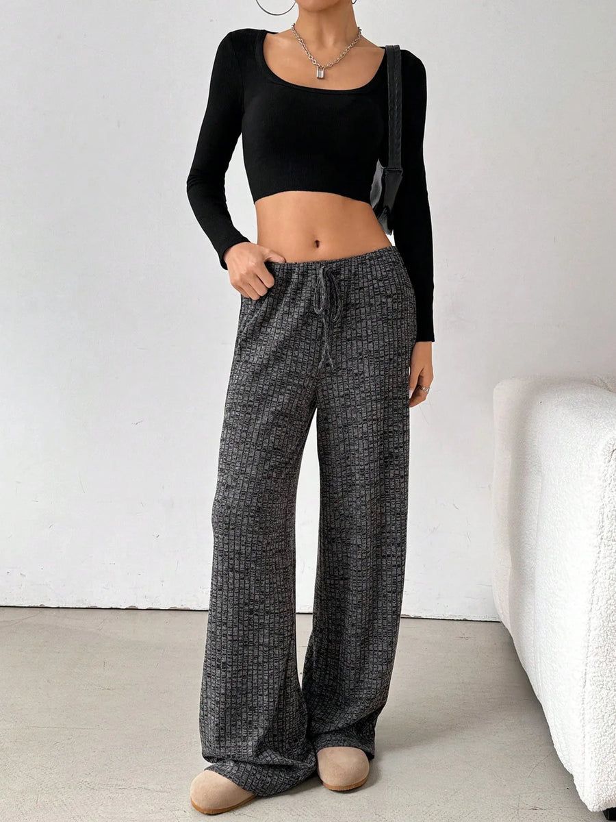 Person wearing black long-sleeve top and gray checkered pants in a minimalistic setting.